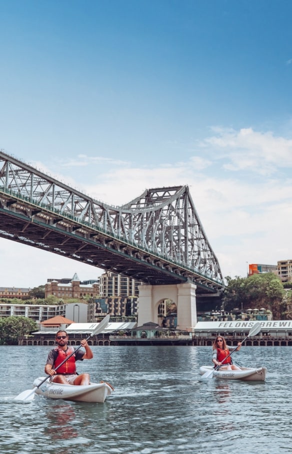 Un homme et une femme faisant du kayak avec Riverlife sur le fleuve Brisbane River et passant sous le Story Bridge avec Howard Smith Wharves en arrière-plan à Brisbane, Queensland © Tourism and Events Queensland