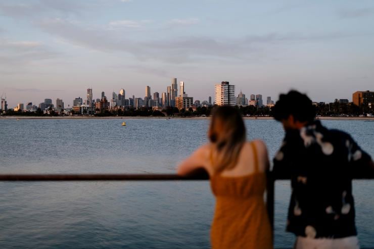 Ein Mann und eine Frau bewundern vom St Kilda Pier aus die Aussicht auf die in der Ferne liegende Stadt, Melbourne, Victoria © Visit Victoria