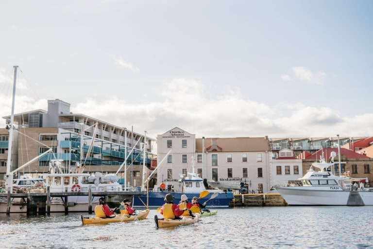 A group of people in yellow kayaks paddle among boats in a marina with Roaring 40s Kayaking  in Hobart, Tasmania © Tourism Australia