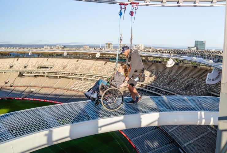 Femme en fauteuil roulant équipée d'un harnais et poussée le long d'une passerelle suspendue lors de l'attraction Ozone à l'Optus Stadium, Perth, Australie Occidentale © Tourism Western Australia