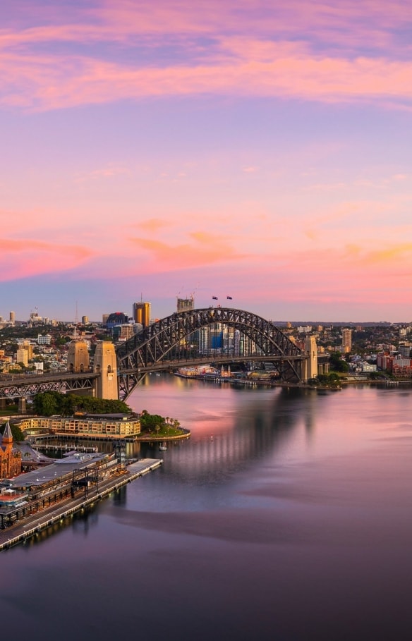 Vue aérienne de la Baie de Sydney réfléchissant les couleurs bleu, rose et doré du coucher au soleil à Sydney, Nouvelle-Galles du Sud © Destination NSW