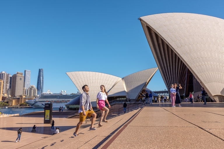 Sepasang wisatawan sedang berjalan-jalan di halaman depan Sydney Opera House, Sydney, New South Wales © Tourism Australia
