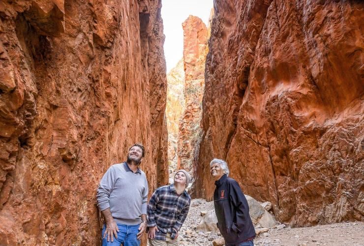 Seorang pria dengan neurodivergensi menjelajahi Standley Chasm dengan pria lain dan pemandu tur, West MacDonnell Ranges, Northern Territory © Tourism NT/Helen Orr