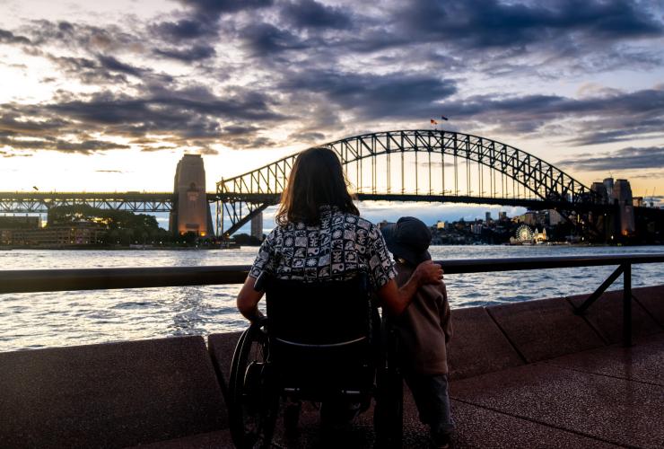 ニュー・サウス・ウェールズ州、シドニー、サーキュラー・キーで、夕暮れ時、息子と一緒にシドニー・ハーバーブリッジを眺める車椅子の男性