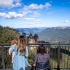 ニュー・サウス・ウェールズ州、ブルー・マウンテンズ国立公園のスリー・シスターズを眺める、車椅子の男性とその家族 © Tourism Australia