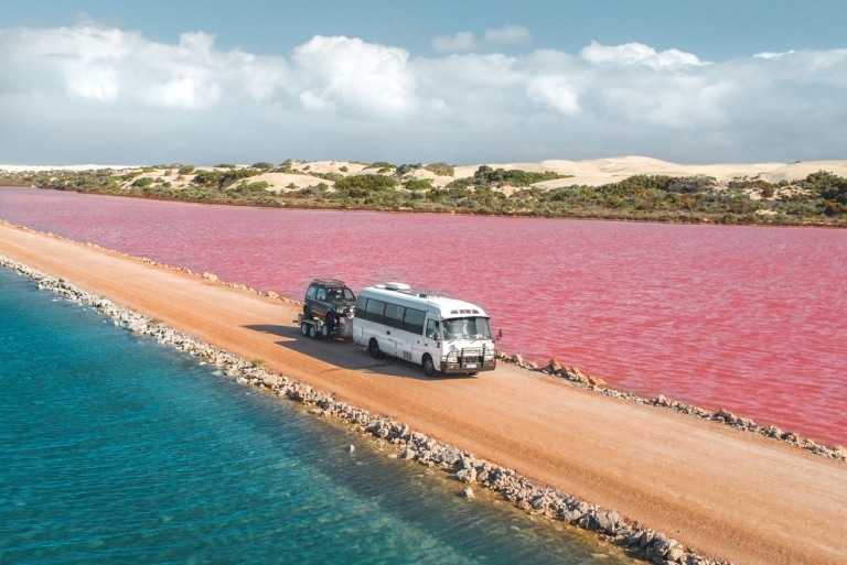 南オーストラリア州、エア半島に広がるピンク色のマクドネル湖とグリーン湖を結ぶ未舗装の道路を走り抜けるバン © Jaxon Foale