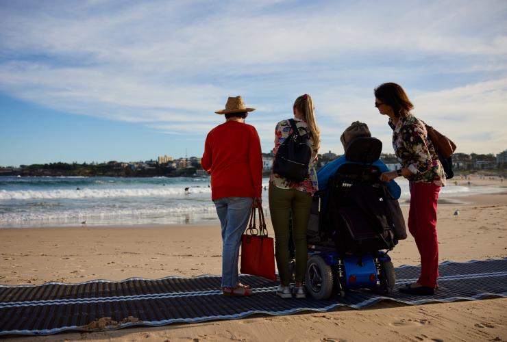 新南威爾士州悉尼邦迪海灘的Australia In Style，一名坐在海灘輪椅上的男士與家人坐在海灘墊上©新南威爾士州旅遊局