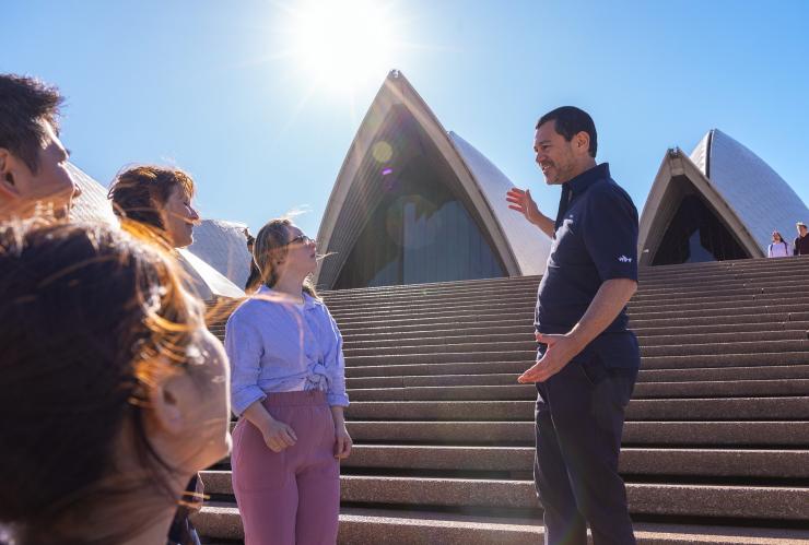 Eine Gruppe Touristen blickt in Richtung der Geste des Reiseführers auf die weißen Segel des Sydney Opera House, Sydney, New South Wales © Tourism Australia