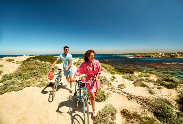 Two people walking their bikes along a sandy path beside the clear blue ocean on Rottnest Island, Western Australia © Georges Antoni