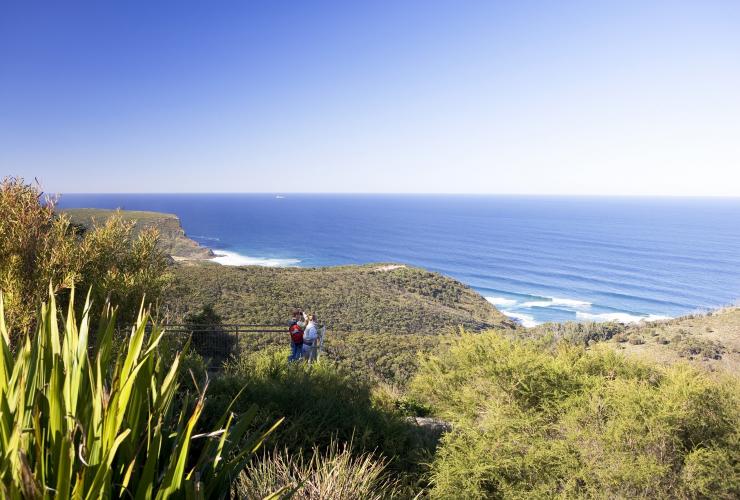 Two people standing at Governor Game Lookout overlooking greenery leading to the ocean in the Royal National Park, Sydney, New South Wales © Destination NSW