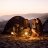 Amis assis autour d'une lampe sur une plage au coucher du soleil avec des tentes en arrière-plan, Tunkalilla Beach, Fleurieu Peninsula, Australie du Sud © South Australian Tourism Commission/Peter Fisher