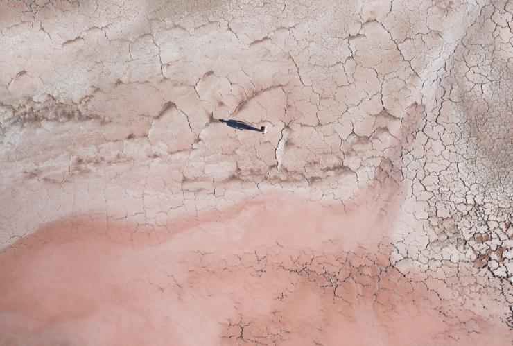 南オーストラリア州、エア半島にあるピンク色の水を湛えたマクドネル湖の乾燥した湖畔に立つ人物から伸びる影を捉えた空撮 © Tourism Australia