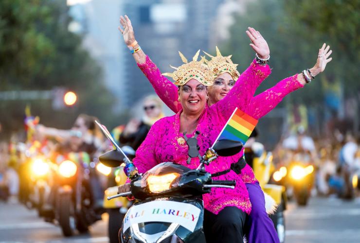 시드니 마디그라에서 왕관과 밝은 분홍색 셔츠를 입은 두 사람이 무지개 깃발과 반짝이로 뒤덮인 모터사이클을 타고 가는 모습, 시드니, 뉴사우스웨일스 © 제프리 펭(Jeffrey Feng)