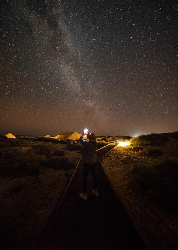 살 살리스 방향으로 걸어가면서 보드워크 위에 서서 별이 빛나는 밤하늘 사진을 찍고 있는 사람의 모습, 닝갈루 리프, 서호주 © 살 살리스 닝갈루 리프