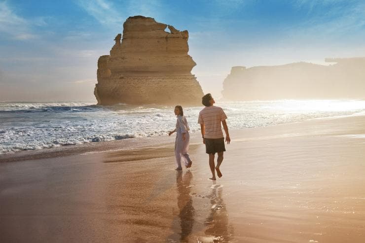 Couple walking along the beach with the twelve apostles in the background © Tourism Australia