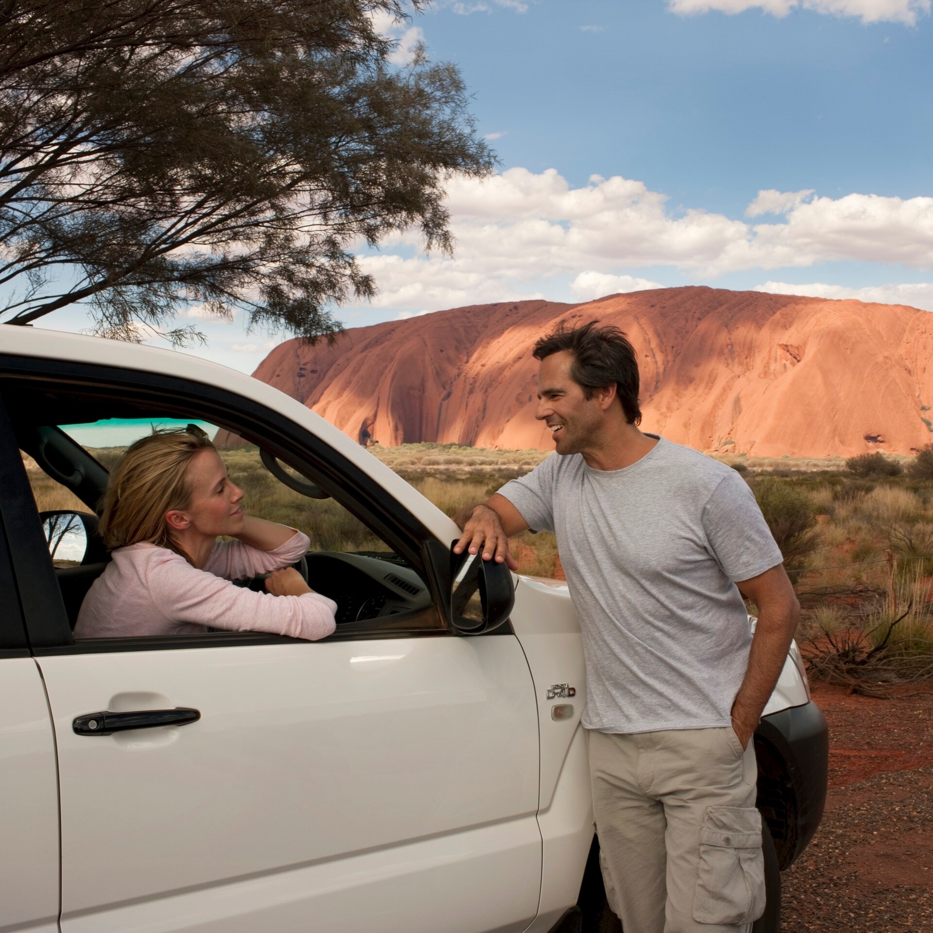 Paar in einem Auto, das neben dem Uluṟu geparkt ist © Tourism Australia