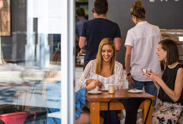 Eine Gruppe von Freunden unterhält sich lachend beim Kaffee in einem gut besuchten Café, Exchange Specialty Coffee, Adelaide, Südaustralien © South Australian Tourism Commission