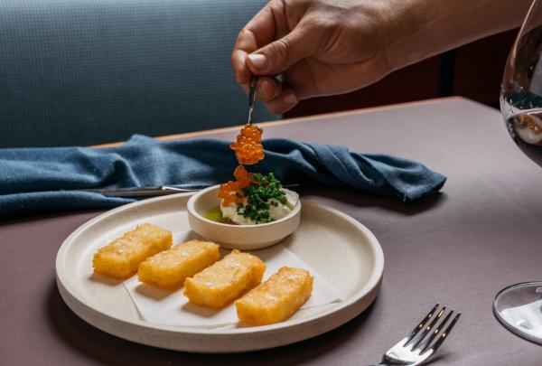 Nahaufnahme einer Hand, die orangefarbenen Fischrogen auf einen sorgfältig angerichteten Teller legt, Fugazzi Bar &amp; Dining Room, Adelaide, Südaustralien © Julian Cebo