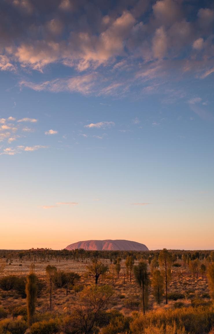 Ein großer Monolith aus rotem Fels erhebt sich aus der flachen Outback-Landschaft am Uluru, Uluru-Kata Tjuta National Park, Northern Territory © Tourism Australia