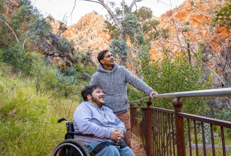 Ein Mann in einem Rollstuhl und ein anderer Mann blicken in die Schlucht Standley Chasm, West MacDonnell Ranges, Northern Territory © Tourism NT/Helen Orr