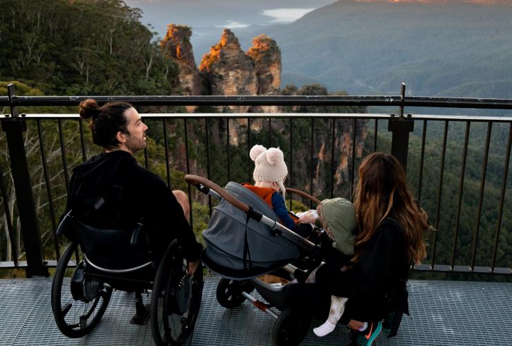 Ein Mann in einem Rollstuhl mit seiner Frau und seinen Kindern mit Blick auf die Three Sisters, Blue Mountains, New South Wales © Tourism Australia