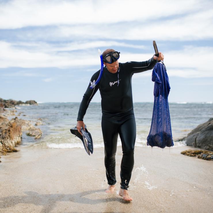 Mann, der mit seinen gefangenen Meeresfrüchten aus dem Meer steigt © Robert Lang/Australian Coastal Safaris