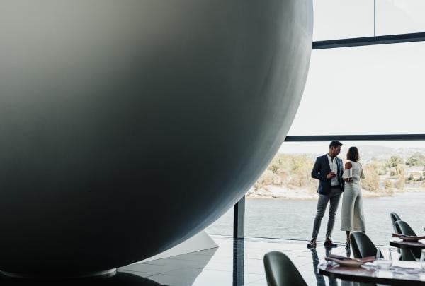 Wein trinkendes Paar, das neben einer Ausstellung im Museum of Old and New Art in Hobart steht © Adam Gibson