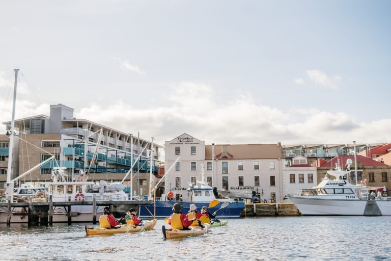 Eine Gruppe von Personen in gelben Kajaks paddelt zwischen Booten in einem Jachthafen mit Roaring 40s Kayaking in Hobart, Tasmanien © Tourism Australia