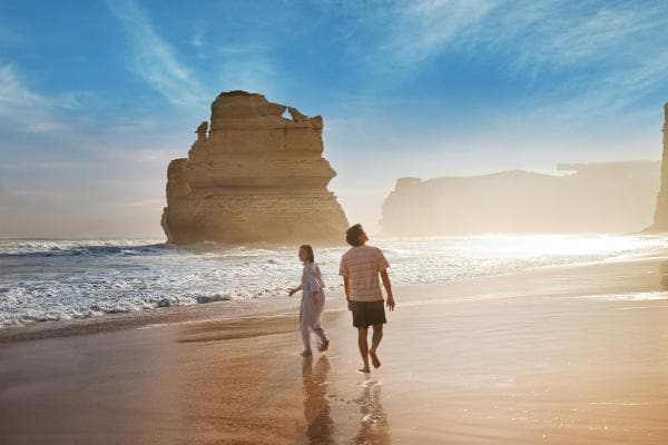 Couple walking along the beach with the twelve apostles in the background © Tourism Australia