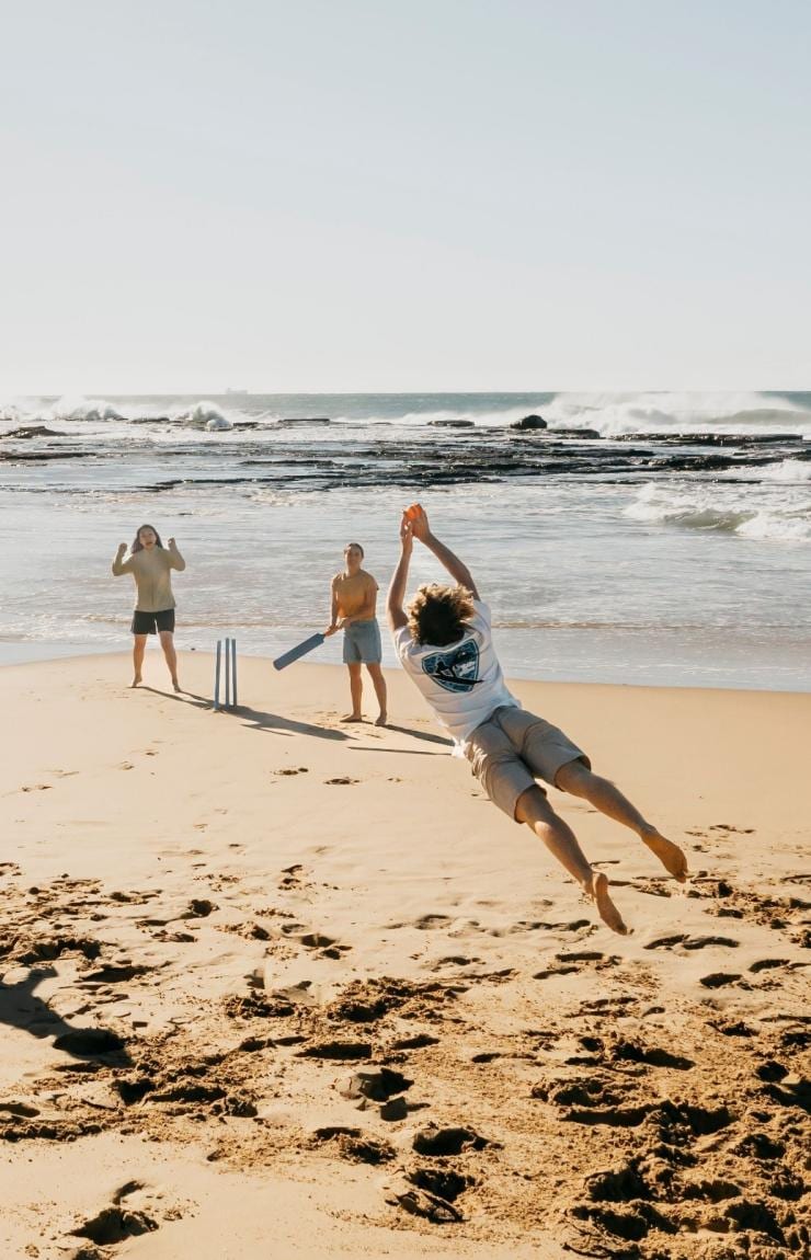 A group of friends playing cricket on the sand at Coledale Beach, Thirroul, New South Wales © Destination NSW 