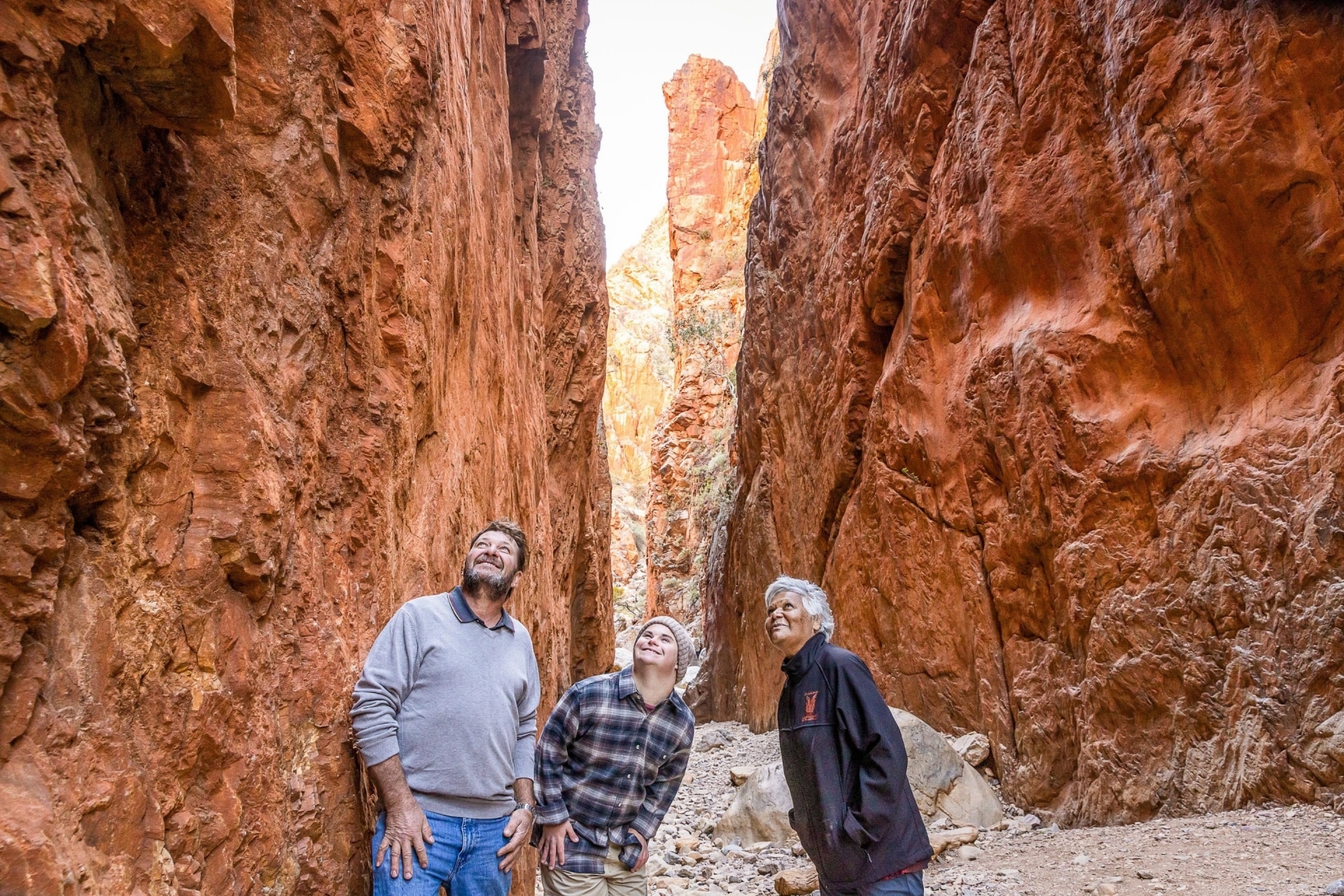 Man with neurodivergence accompanied by another man and a tour guide at Standley Chasm, West MacDonnell Ranges, Northern Territory © Tourism NT/Helen Orr