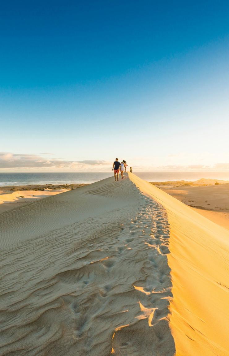 A group of people walking on a towering sand dune towards the distant ocean, Gunyah Beach Sand Dunes, Eyre Peninsula, South Australia © South Australian Tourism Commission