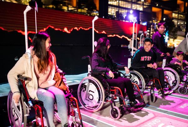 A group of friends seated in wheelchairs in a reserved area, with colourful lights surrounding them at Vivid Sydney, New South Wales © Destination New South Wales