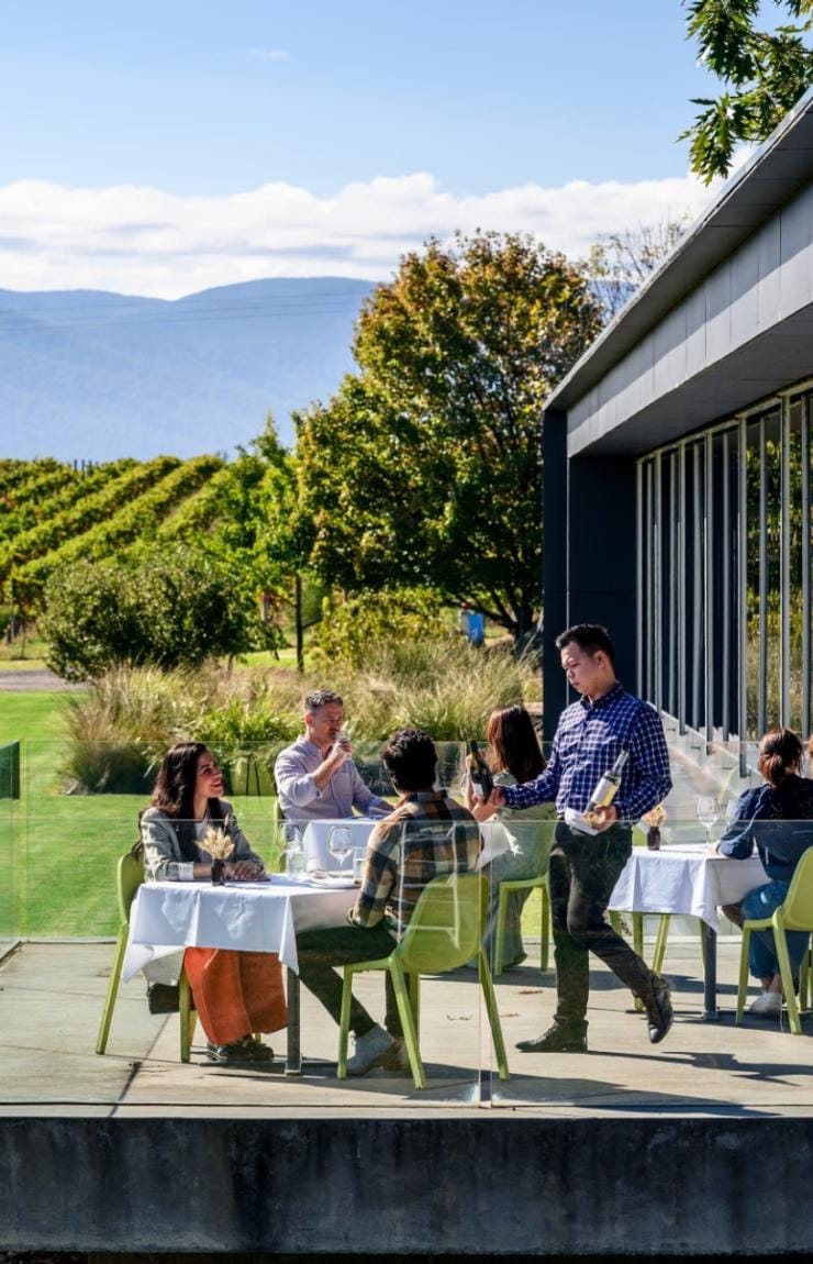 People dining and drinking wine on a terrace overlooking a lush green vineyard, Oakridge Wines, Yarra Valley, Victoria © Visit Victoria