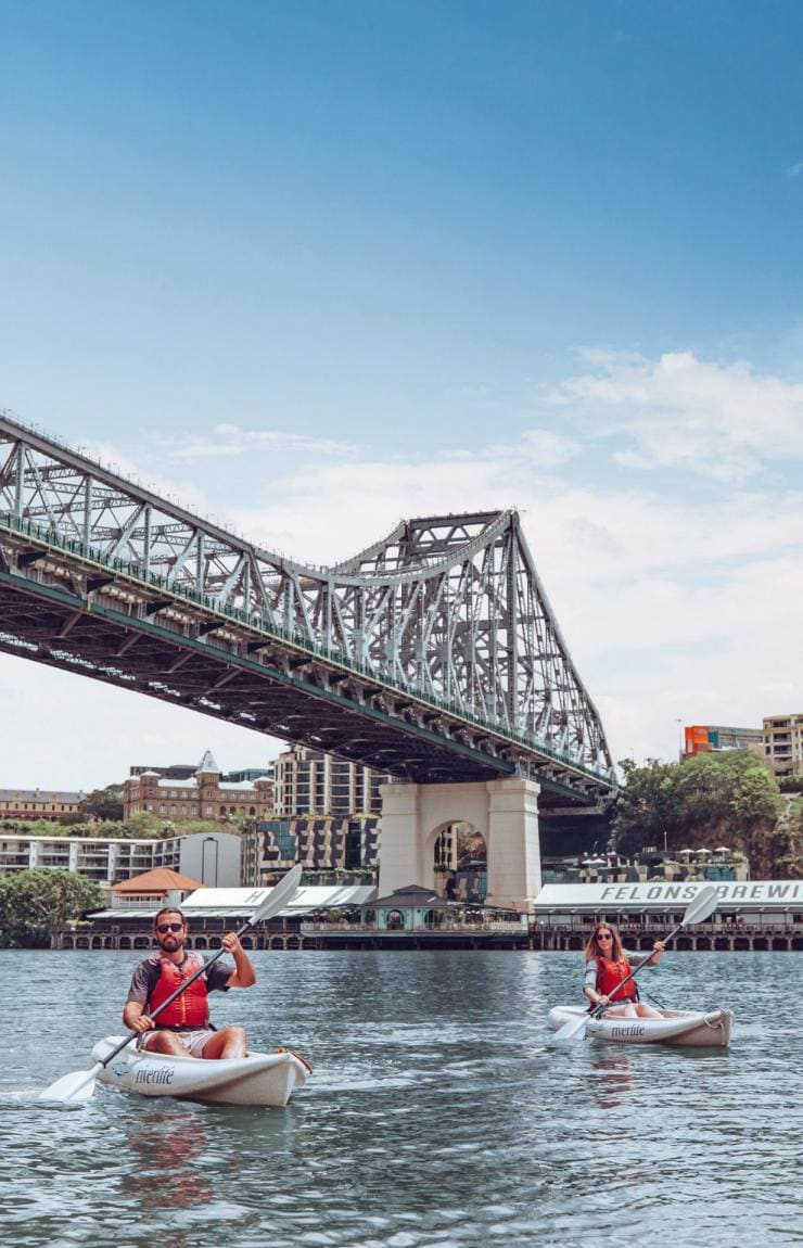 A man and woman kayaking with Riverlife along Brisbane River beneath Story Bridge with Howard Smith Wharves in the background in Brisbane, Queensland © Tourism and Events Queensland
