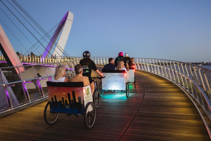 A group of people riding in rickshaws pulled by tour guides on bikes across a waterfront boardwalk during sunset with Peddle Perth, Perth, Western Australia © Tourism Australia A group of people riding in rickshaws pulled by tour guides on bikes across a waterfront boardwalk during sunset with Peddle Perth, Perth, Western Australia © Tourism Australia