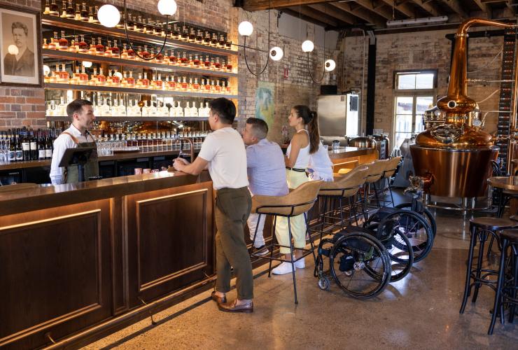 Friends sitting and sampling spirits at Rivermakers precinct with a wheelchair to the side, Brisbane, Queensland © Tourism and Events Queensland