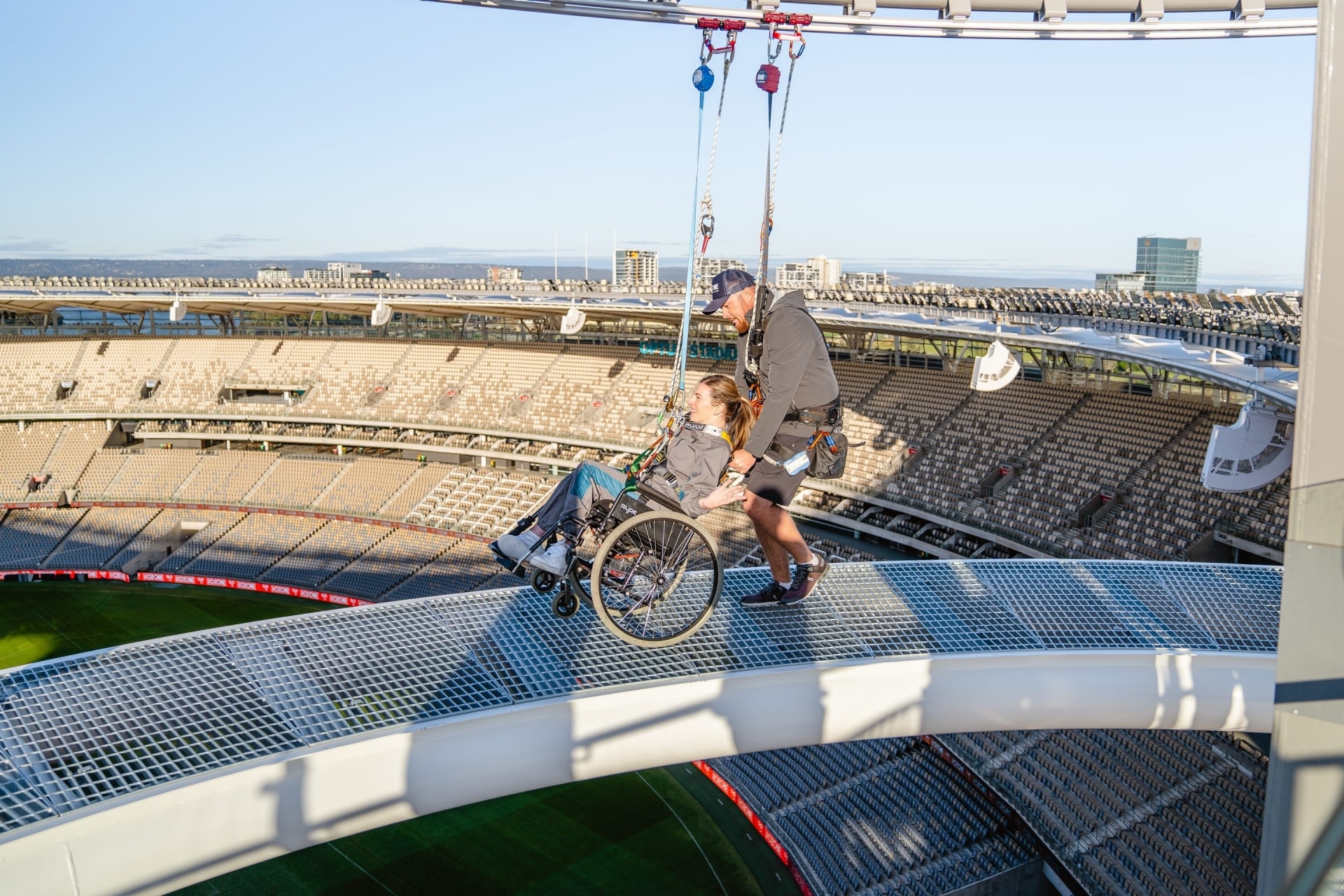 Woman wearing a harness in a wheelchair being guided along a dramatic ledge at the Ozone above Optus Stadium in Perth, Western Australia © Tourism Australia