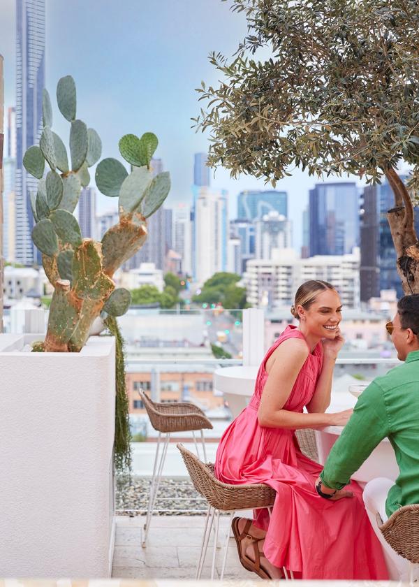 A couple smiling at a table on a rooftop bar overlooking a city skyline, Maya, Brisbane, Queensland © Brisbane Economic Development Agency