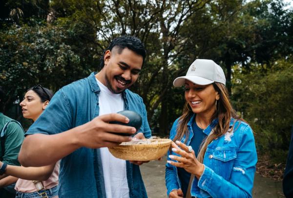 Two people holding a large, green emu egg on a path surrounded by trees, Royal Botanic Garden Sydney, New South Wales © Tourism Australia