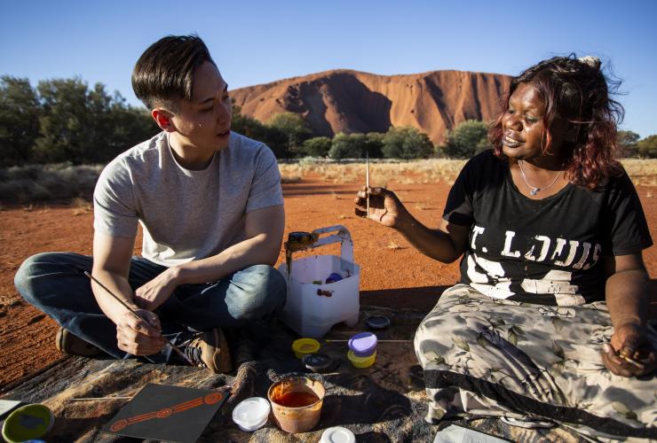 Visitor participates in a dot-painting workshop next to Uluru with Maruku Arts © Tourism Australia
