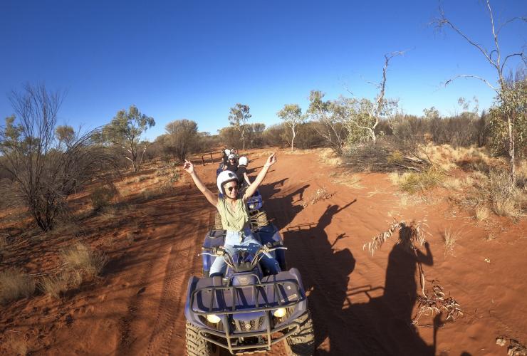 A group of people riding quad bikes through red sand at Kings Creek Station, Kings Canyon, Northern Territory © Tourism Australia