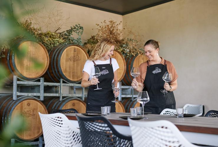 Two waiters laughing together as they set a table with wine glasses in an oak barrel-lined room at Mollydooker Wines, Fleurieu Peninsula, South Australia © South Australian Tourism Commission