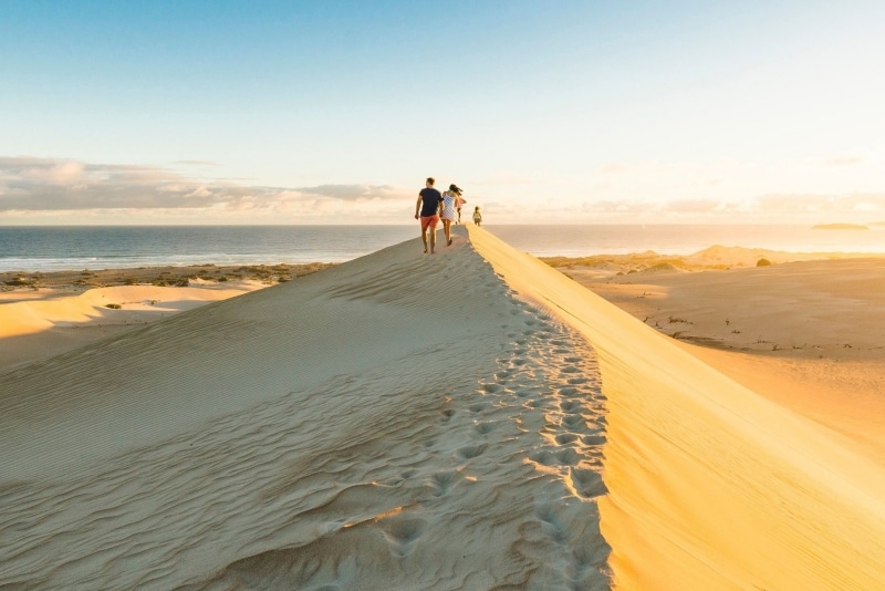 A group of people walking on a towering sand dune towards the distant ocean, Gunyah Beach Sand Dunes, Eyre Peninsula, South Australia © South Australian Tourism Commission