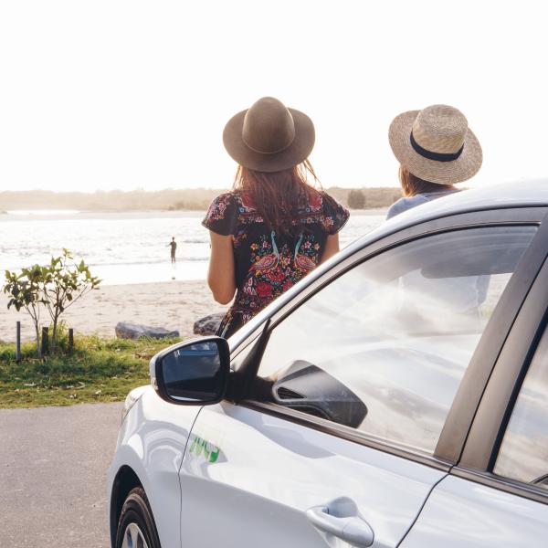 Two girls sat on front of Jucy car looking over the beach in Noosa © Jucy