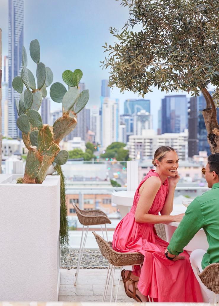 A couple smiling at a table on a rooftop bar overlooking a city skyline, Maya, Brisbane, Queensland © Brisbane Economic Development Agency