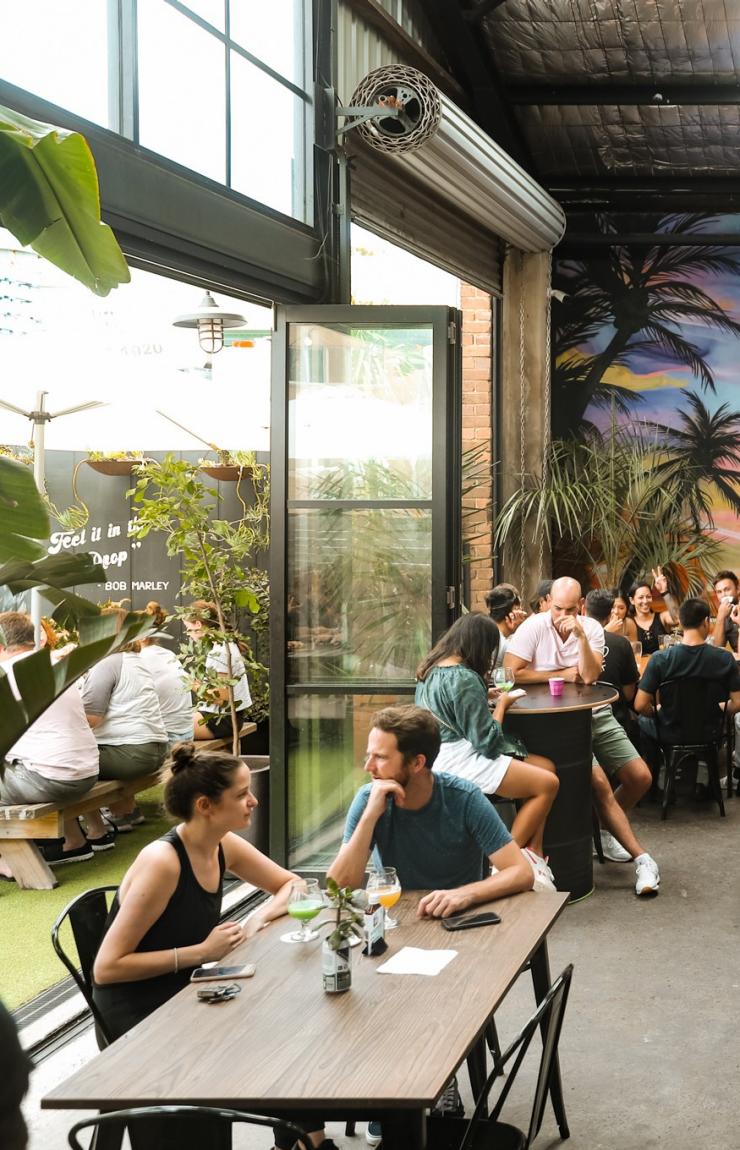 A crowd of people sitting around long tables in a brewery with a colourful mural. at One Drop Brewing, Botany, Sydney, New South Wales © One Drop Brewing Co. 
