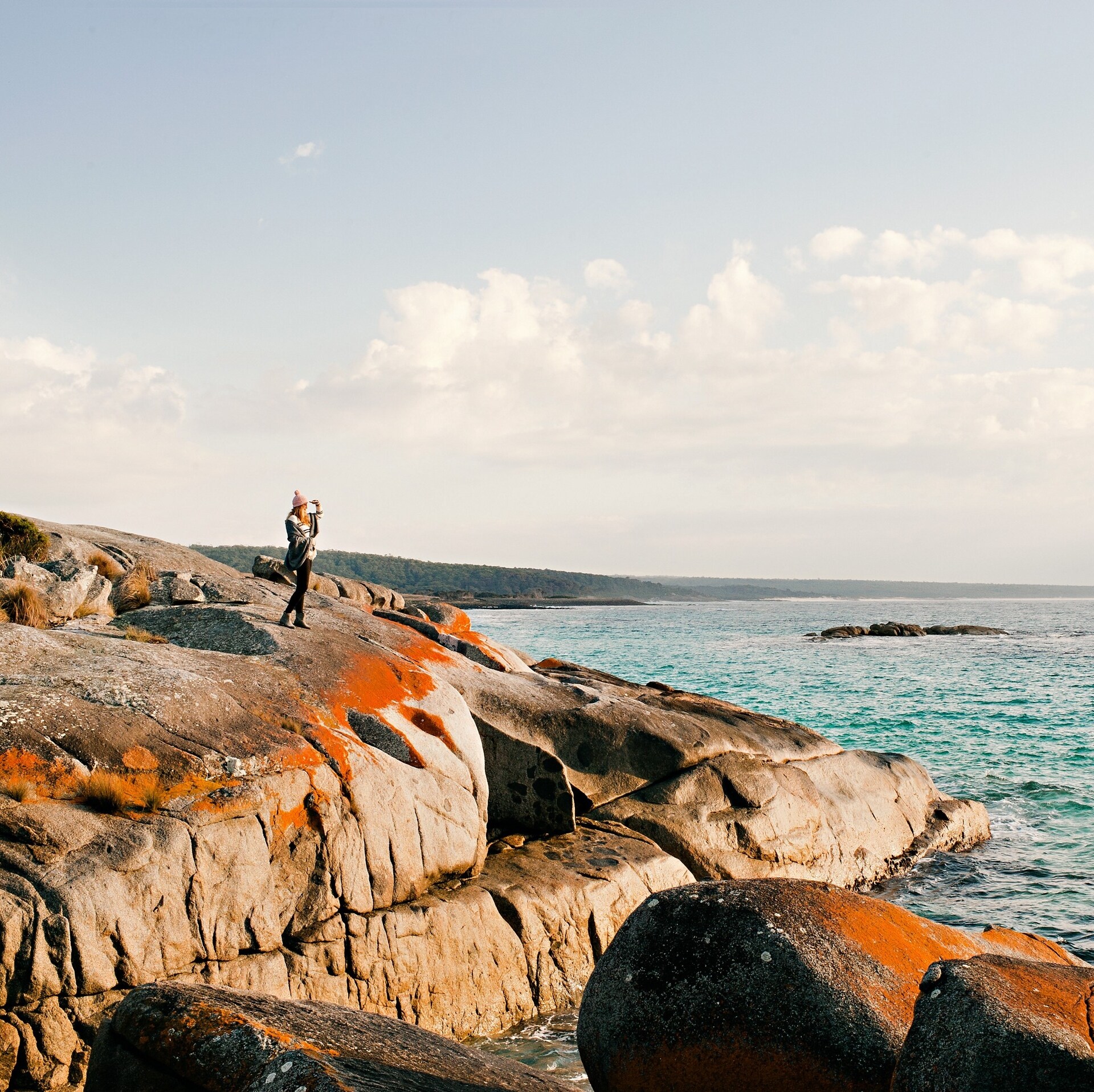 Woman stand on rocks looking out at the ocean at The Gardens in the Bay of Fires Conservation Area © Lisa Kuilenburg