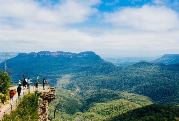 A green valley of the Blue Mountains with the three peaks of the Three Sisters rock formation in view © Destination NSW