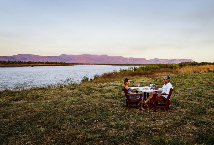 Couple enjoying sunset drinks by the Pentecost River with the Cockburn Ranges in the background, Home Valley Station, WA © Tourism Western Australia